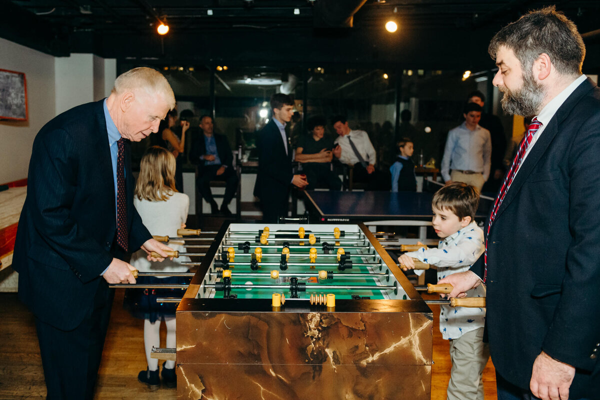A young boy plays foosball with grandpa as dad looks on