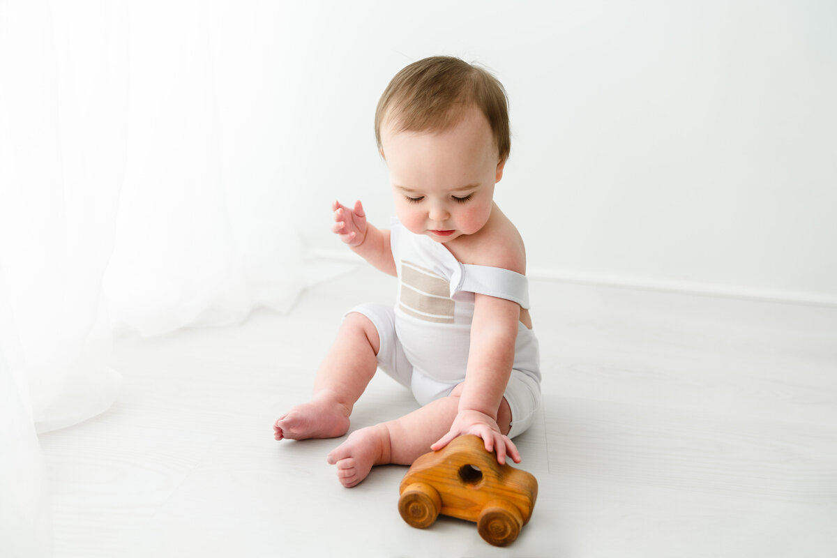 Toddler playing with a wooden toy car on a bright white background. Taken by Fig and Olive Photography, Minneapolis Baby Photographer.
