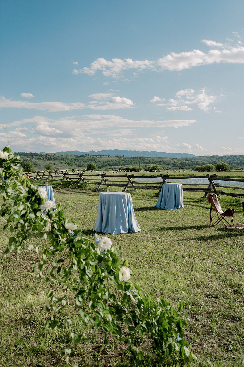 Cocktail tables draped in French blue linen stand gracefully outdoors, framed by the majestic Teton Mountains in the background.