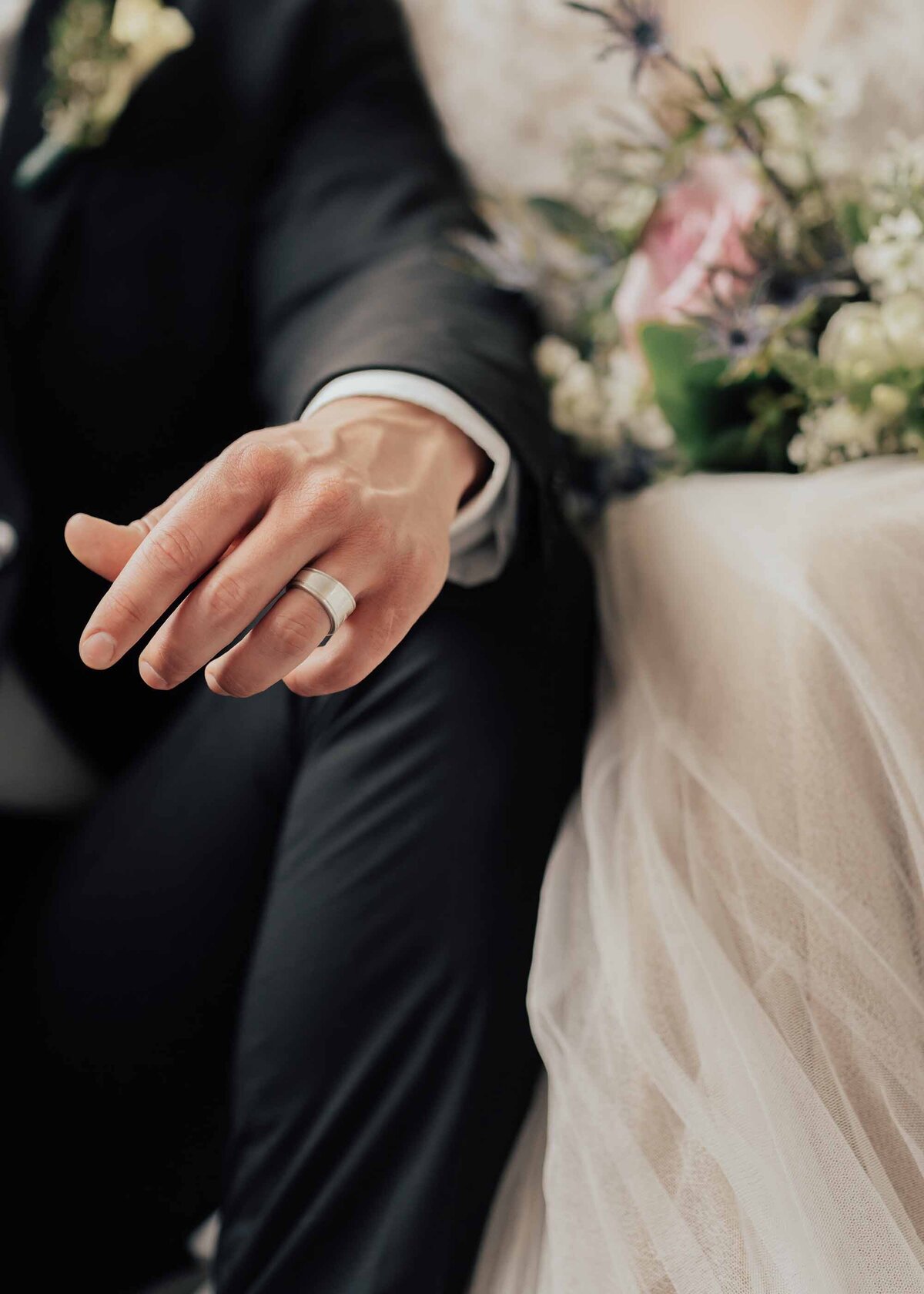 Maddie Rae Photography up close image of grooms ring on his finger. bride and groom are sitting in the background