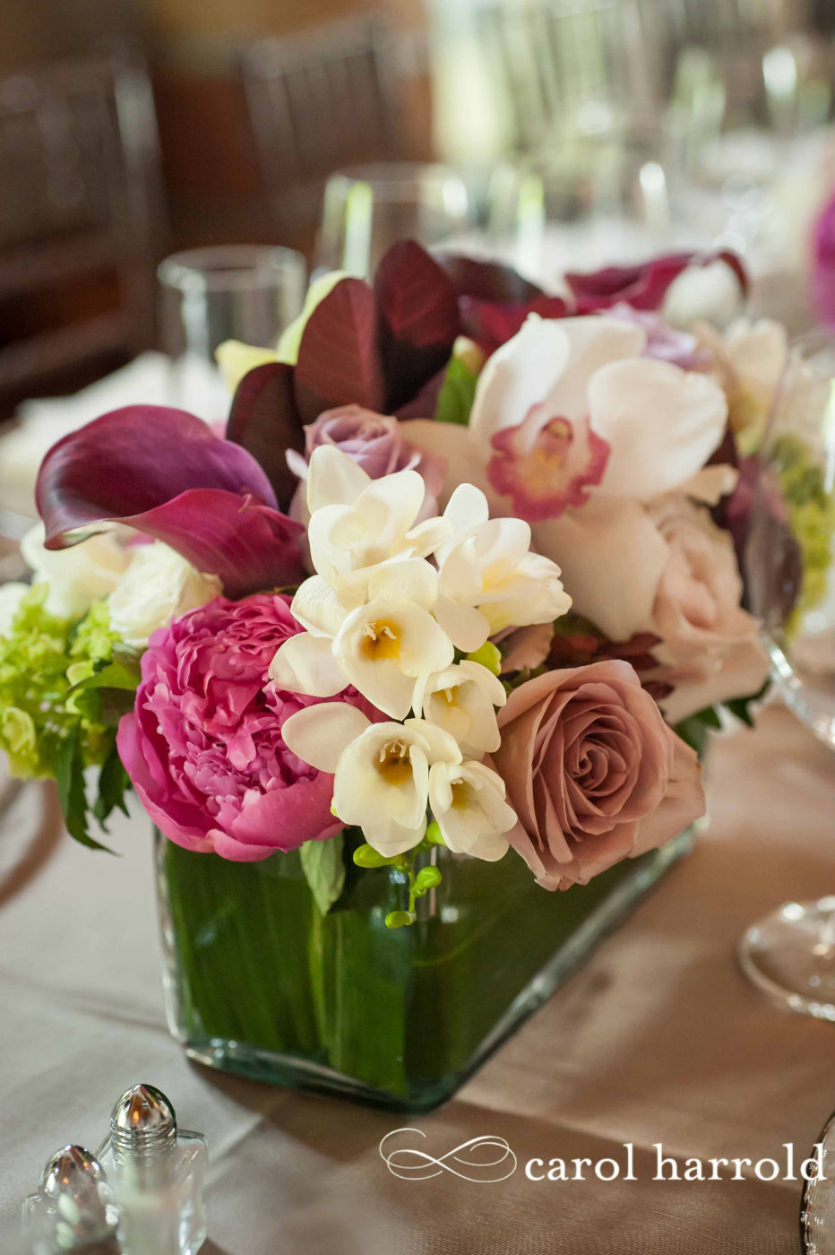modern centerpiece of white freesia, pink peonies, purple calla lilies, mauve roses, white orchids, in leaf lines square glass vase