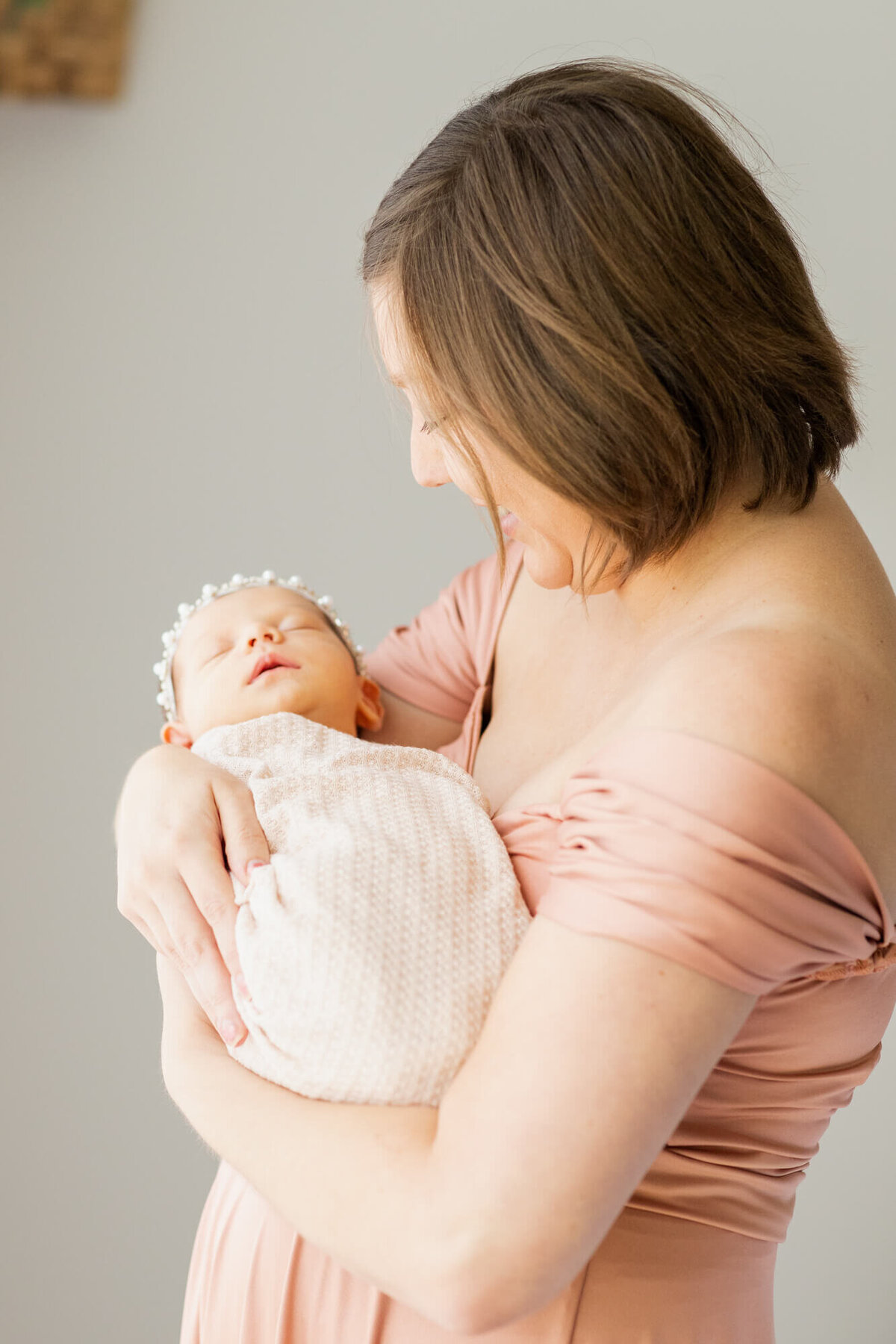 Mom in a peach dress stands and cradles her newborn baby girl