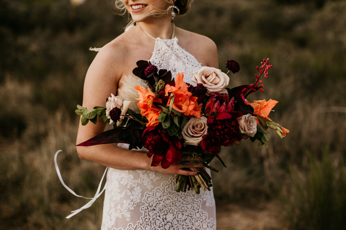 red and orange bouquet in brides arms
