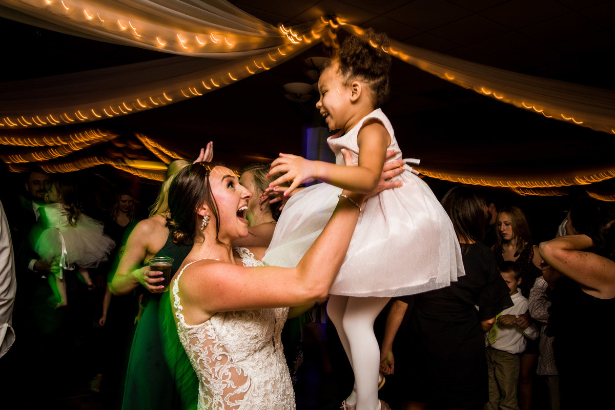 Bride lifts laughing little girl while dancing.