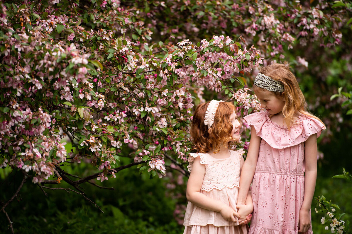 two little girls with red hair and pink dresses smile at each other during family photos in Ottawa