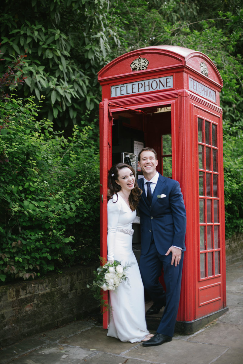 Laughing newlywed couple in a london phone booth