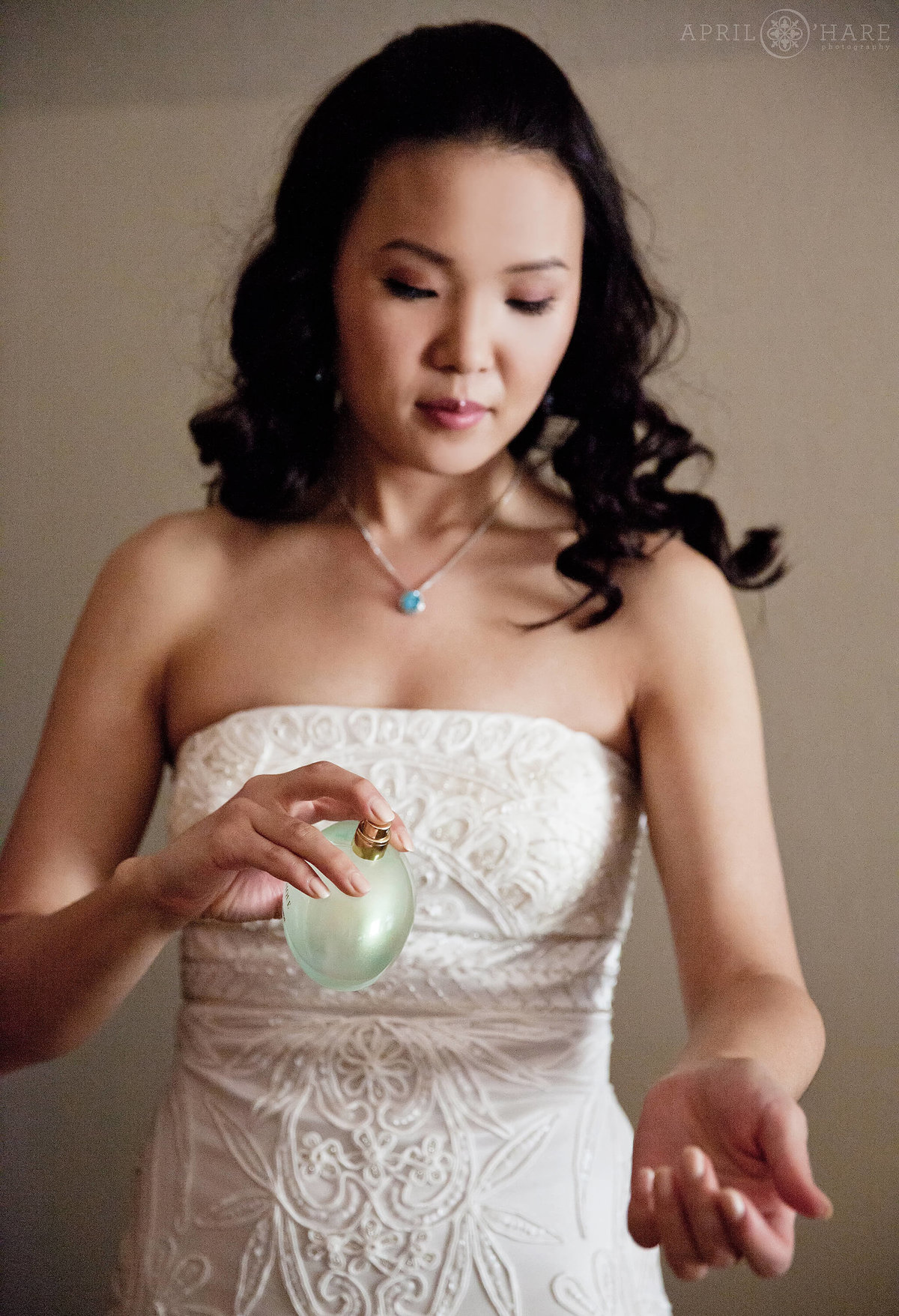 A pretty Asian bride squirts some perfume on the day of her Estes Park wedding at a VRBO house in Colorado