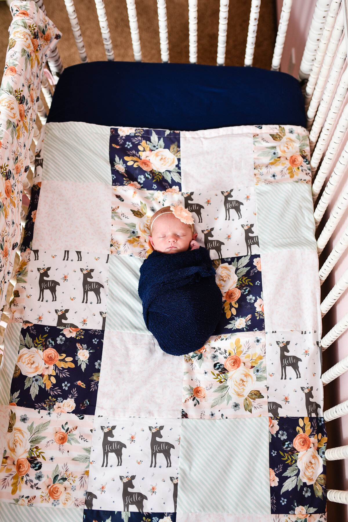 Beautiful  lifestyle newborn photography: Newborn girl wrapped in navy in her crib with cnavy and peach floral bedding