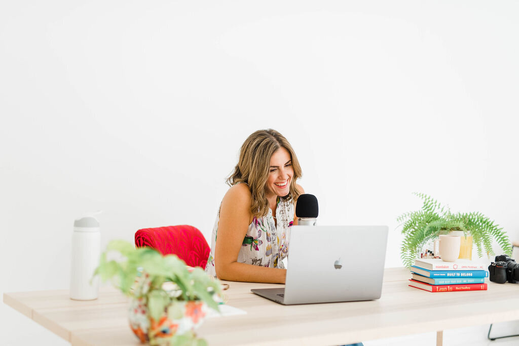 smiling woman looking at laptop with podcast mic
