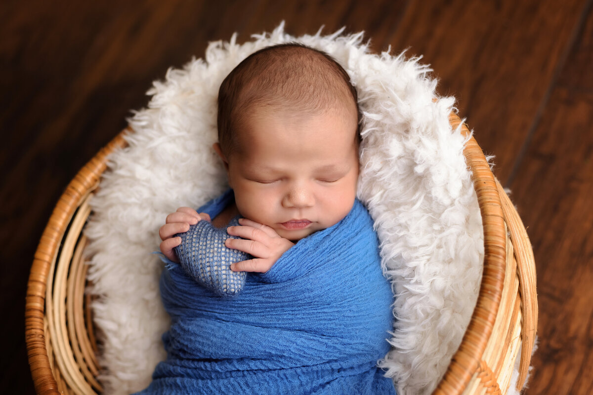 Newborn Photographer, a baby sleeps swaddled in a blanket and cozy in a basket