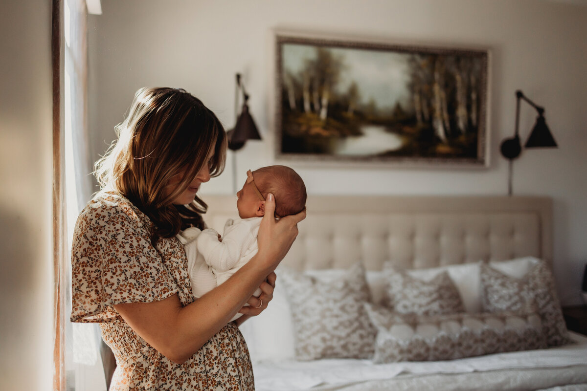 mom snuggles new baby in  neutral master bedroom