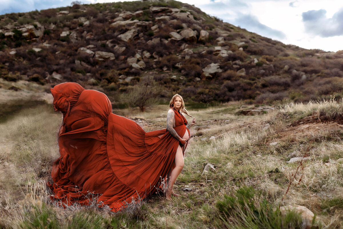 mom in gorgeous rust gown on the mountain top in colorado posed for her maternity portraits
