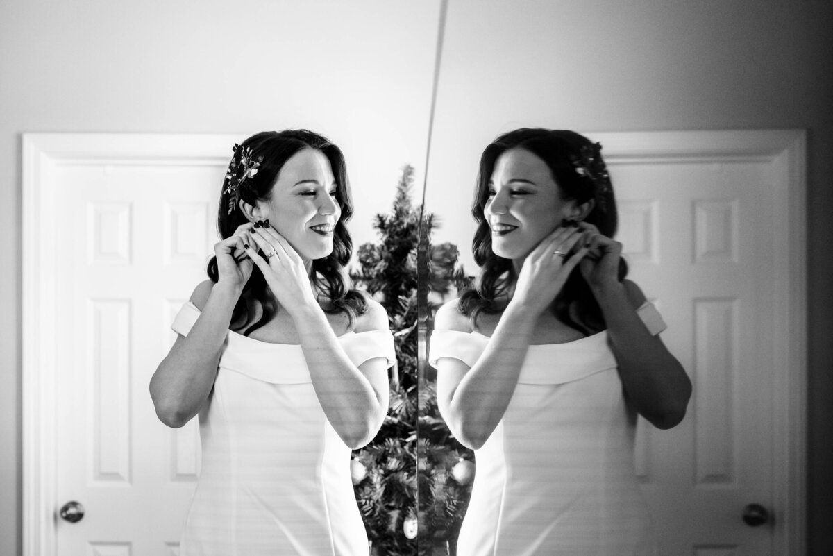 Black-and-white-image-symmetrically-reflecting-bride-as-she-puts-on-her-earrings