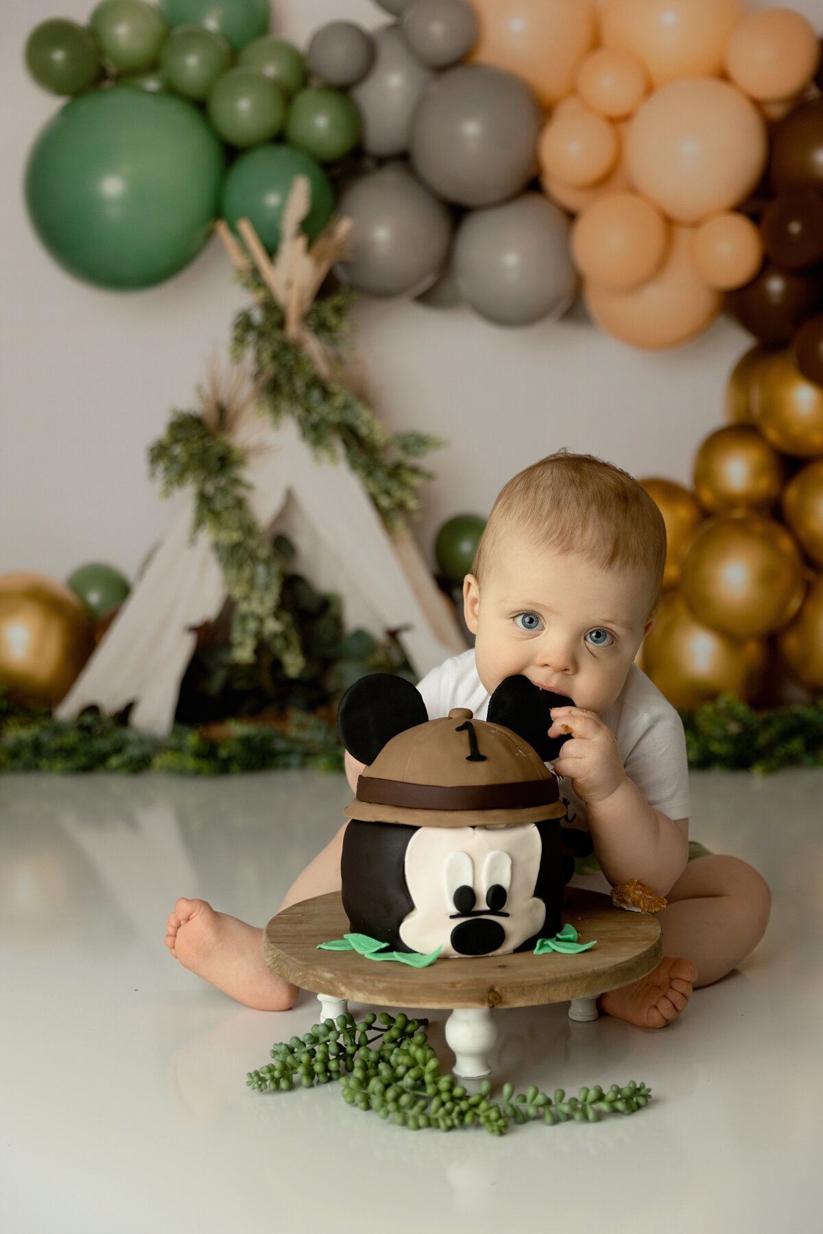 A young boy bites the ear of his mickey mouse cake in a studio