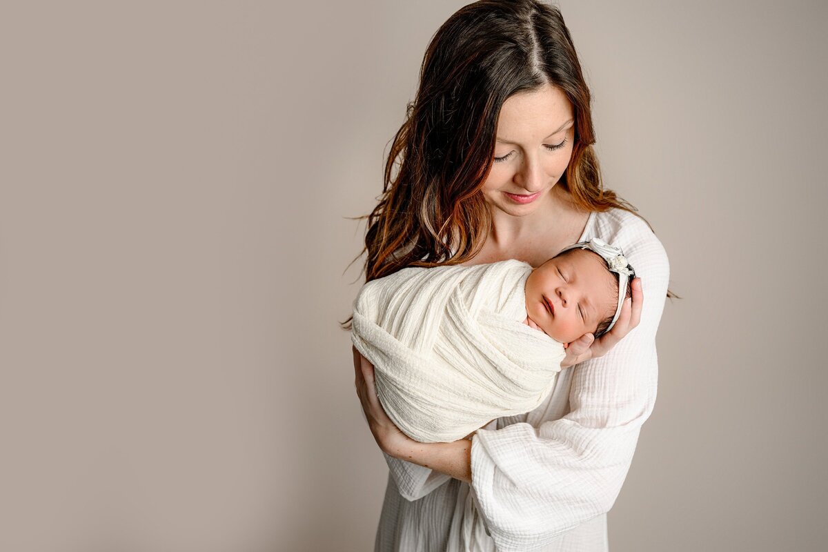 mother dressed in cream looks down at her infant daughter wrapped in cream