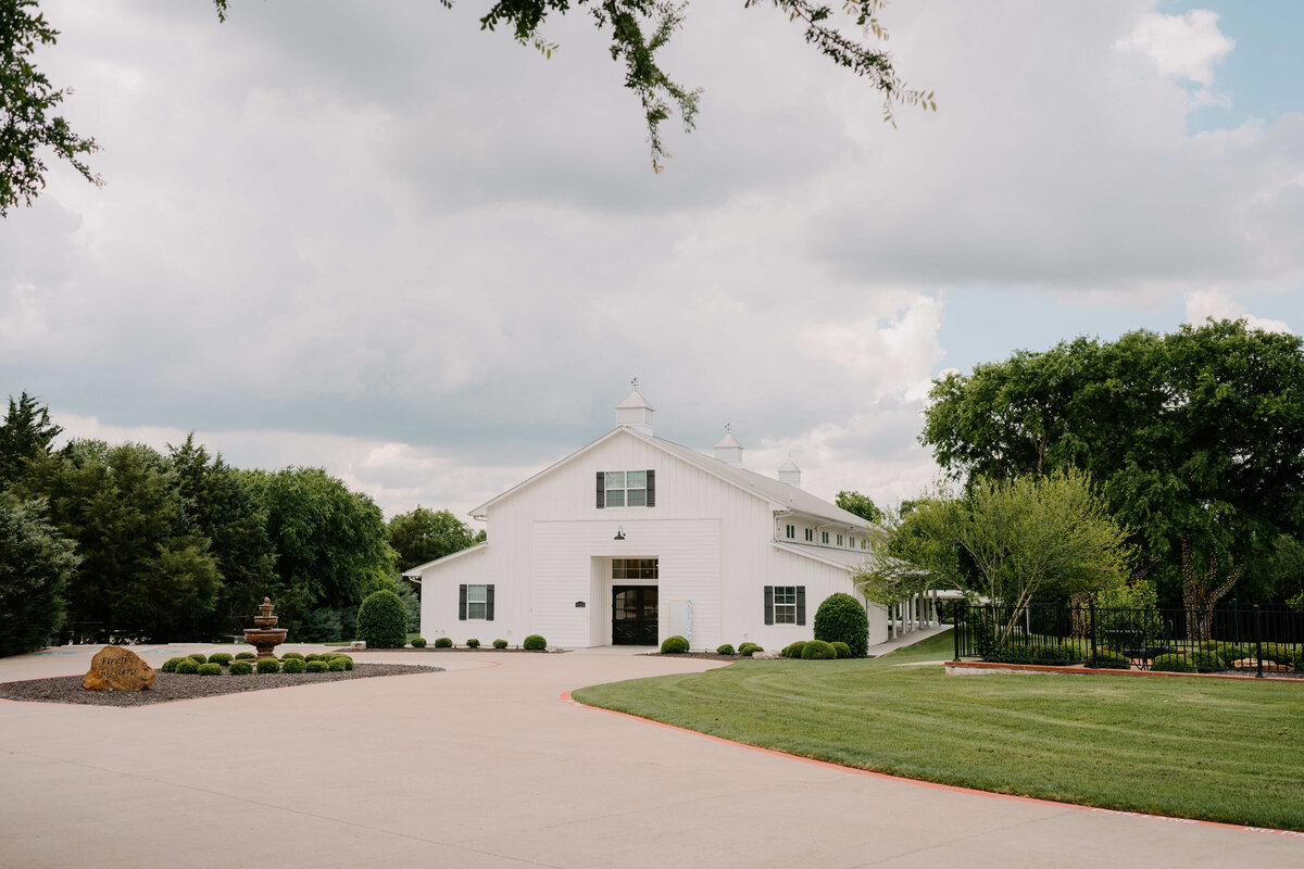 A large white barn stands in a lush green landscape under a partly cloudy sky, exuding a serene and picturesque rural charm.