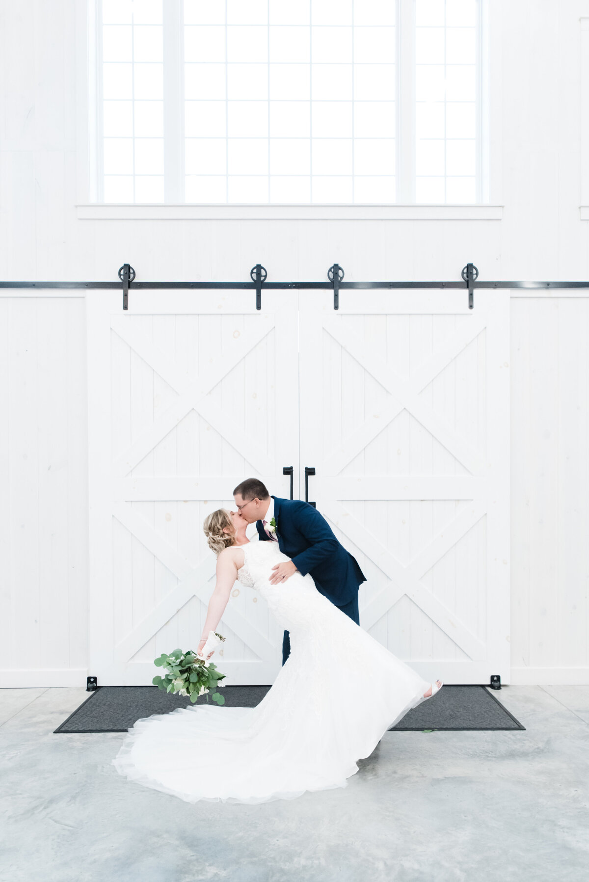 groom dips bride and kisses her in front of barn doors of the grayson house