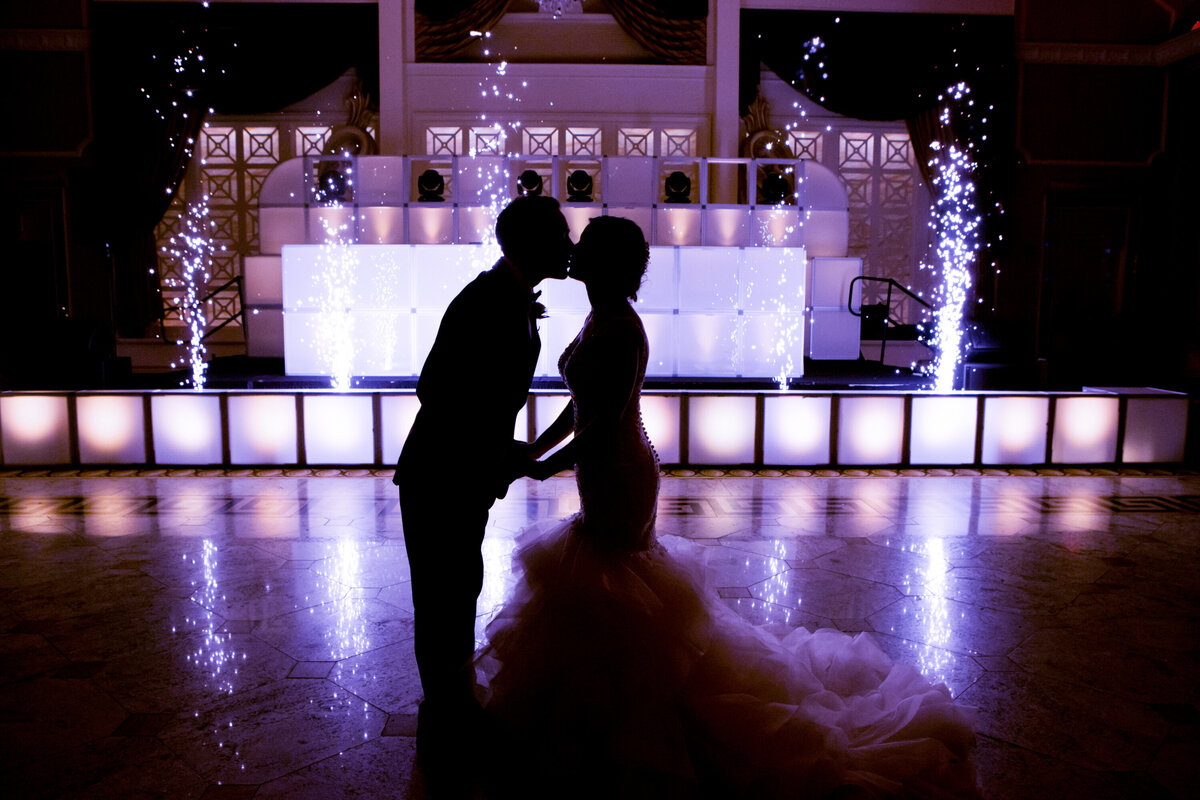 Bride and groom kiss in silhouette on purple uplighting dance floor with sparklers Venetian New Jersey wedding photographer Milestone Images
