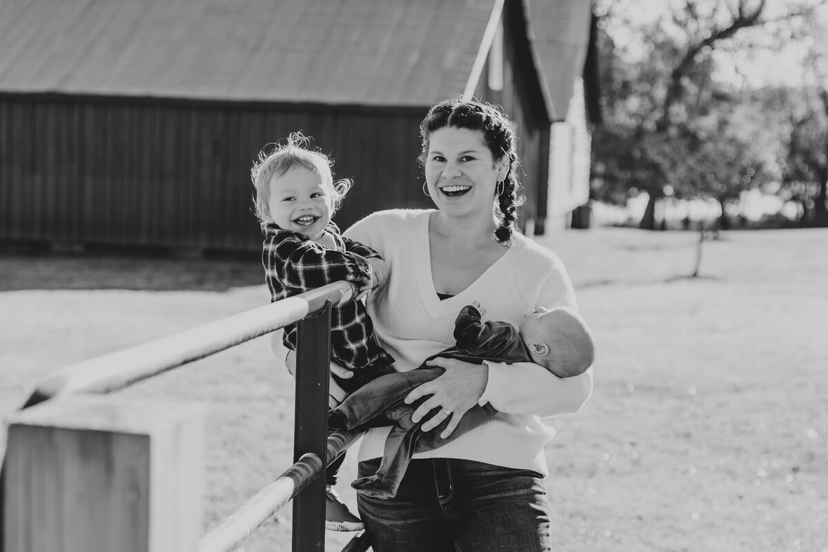Family with New Baby and Toddler, standing in front of Red Barns for Updated Family Photos at Windsor Castle Park in Smithfield Virginia at Sunrise in Fall - Rebekah Heffington Photography