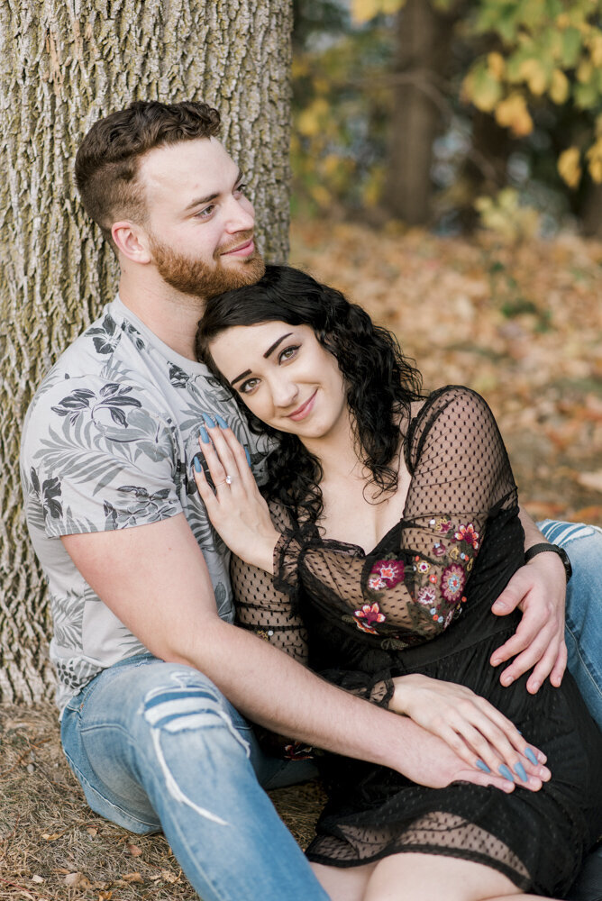 engaged couple sitting by a tree
