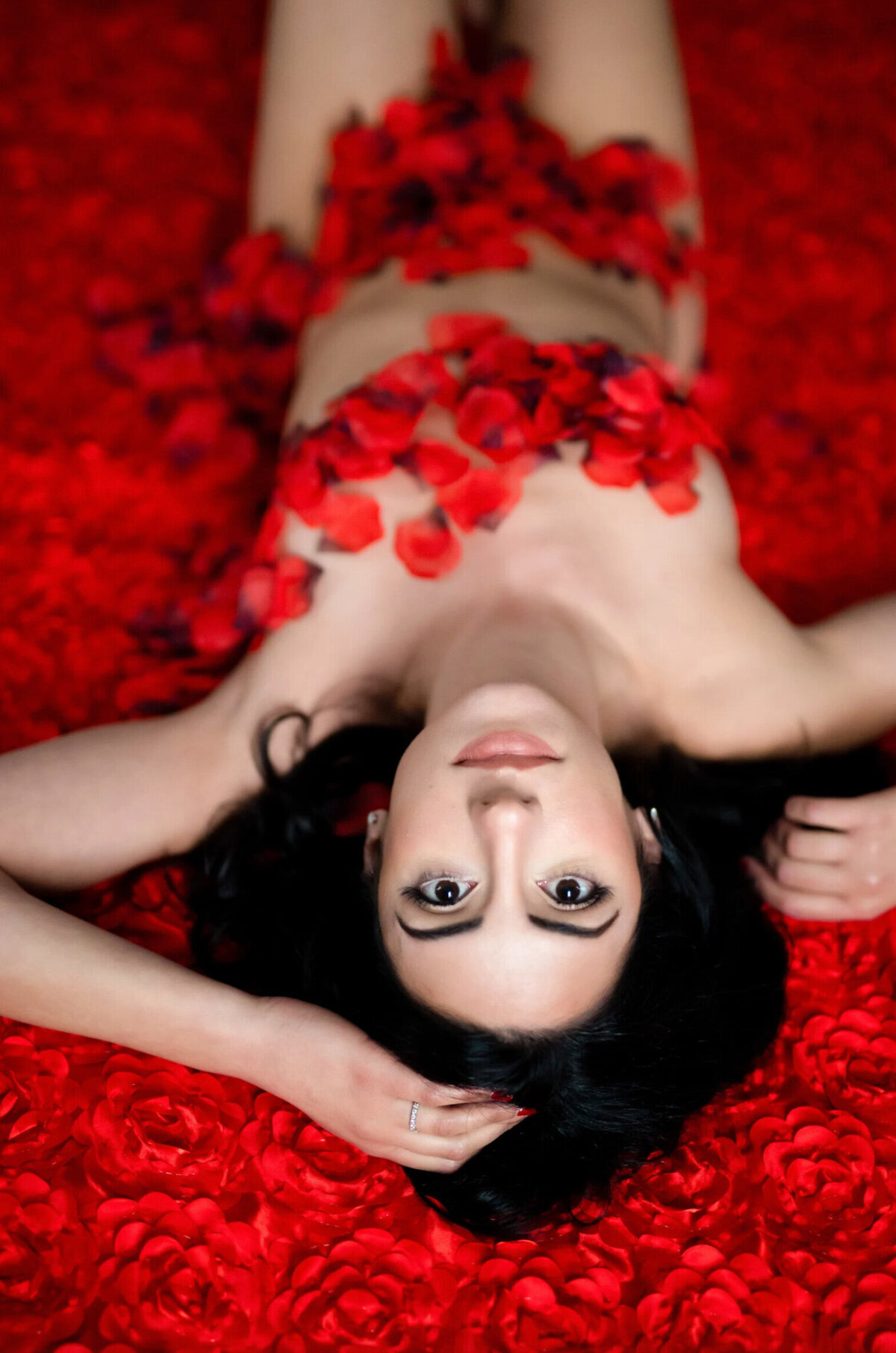 Woman covered in red rose, petals posing for a boudoir photo shoot
