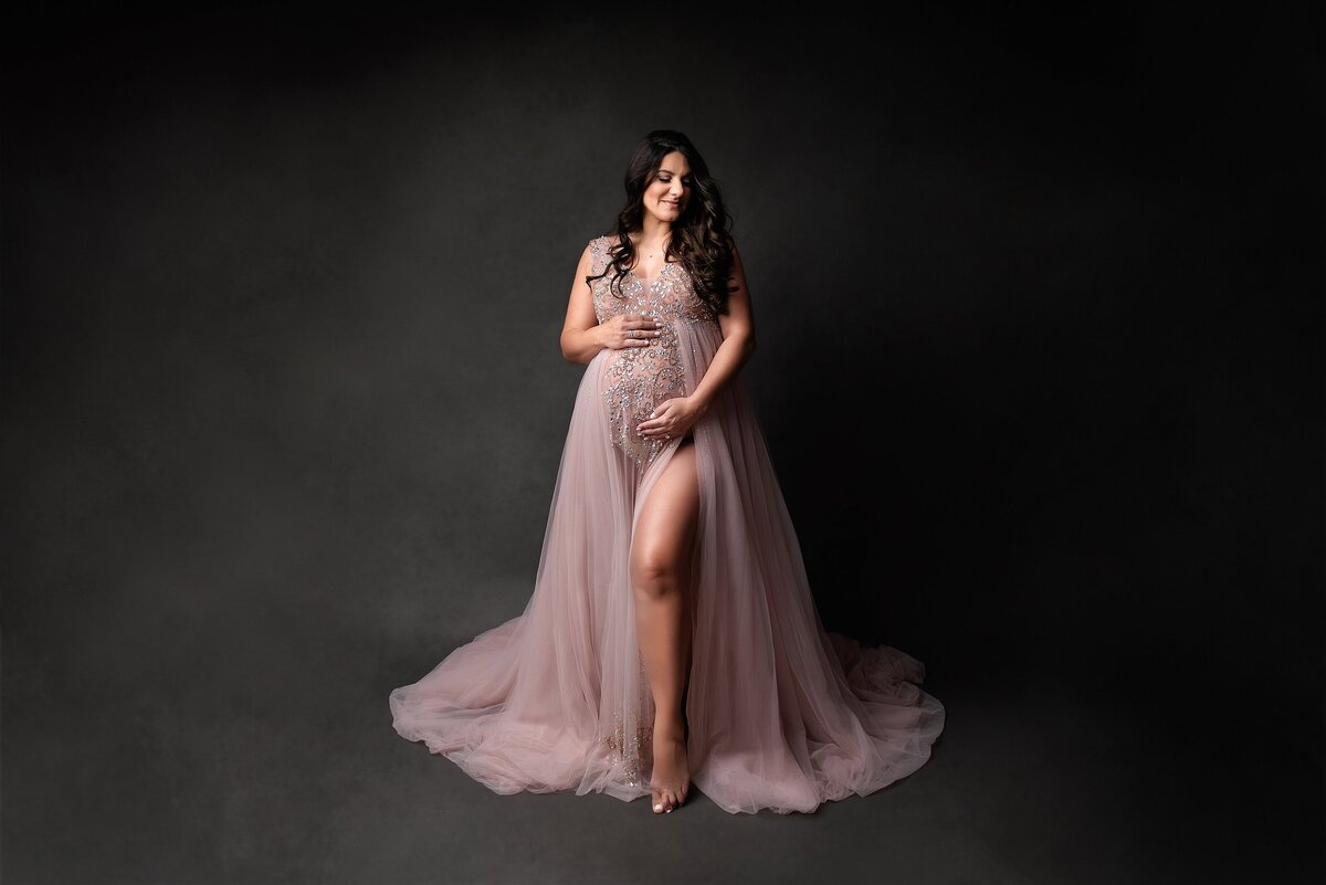 Pregnant model poses in pink couture gown from client closet for her maternity photoshoot.