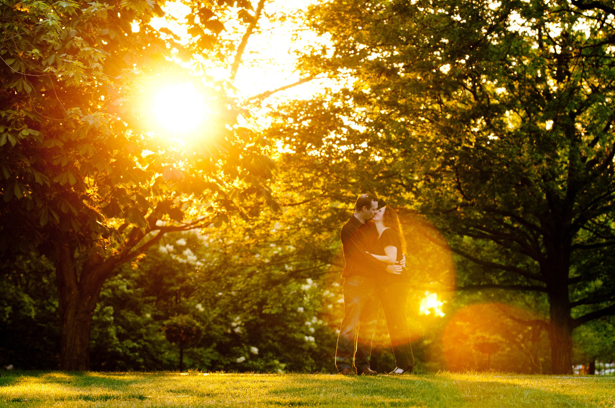 Kissing engagement couple enveloped in a sun flare