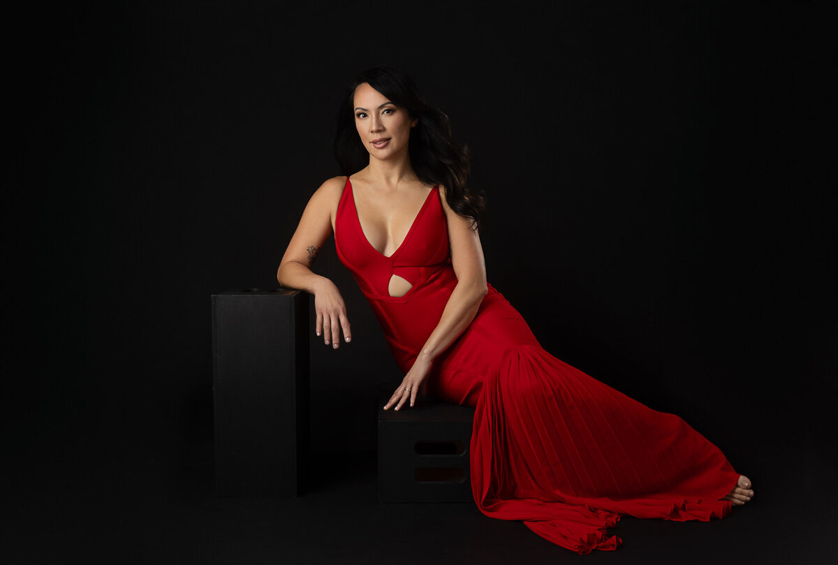 asian woman in her 40's is having her picture taken in a studio over black backdrop and she's wearing a beautiful red dress at Ingrid Barnhart Photography in Austin, Texas