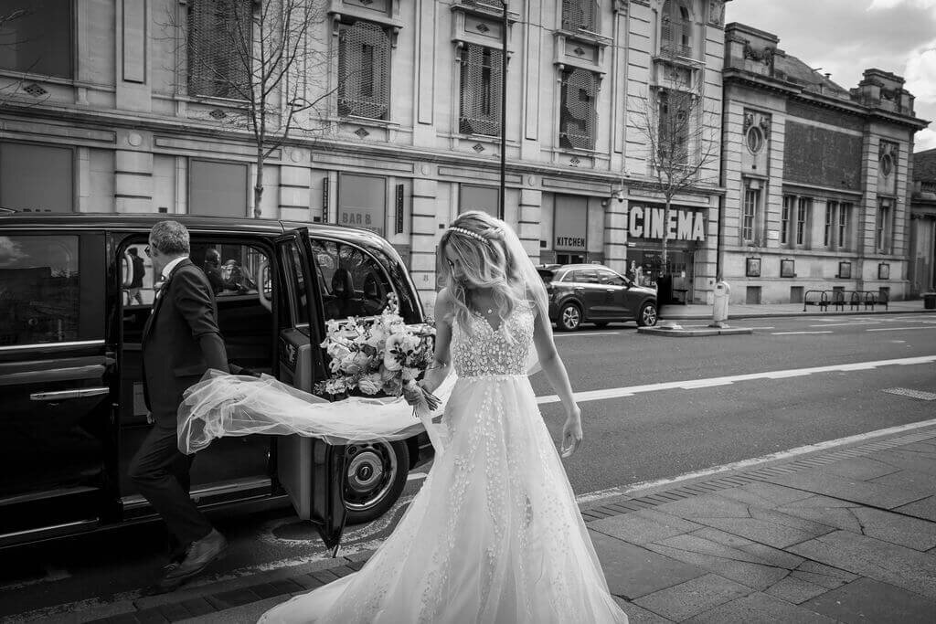 Brides veil blows in the wind as she steps out of a Black cab