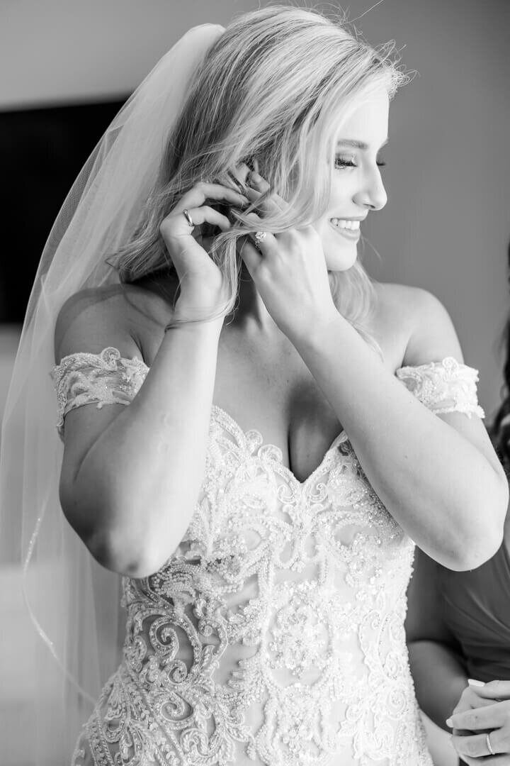 B&W fine art wedding photography of a close up of a bride putting on her earring as she looks out the window. Captured at The Venue at Oakdale in North Little Rock, AR.