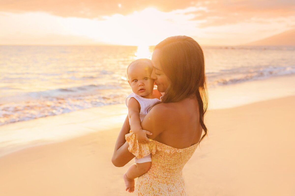 Beautiful mother in yellow sun dress cuddles her baby on the beach in Wailea with Love + Water Photography
