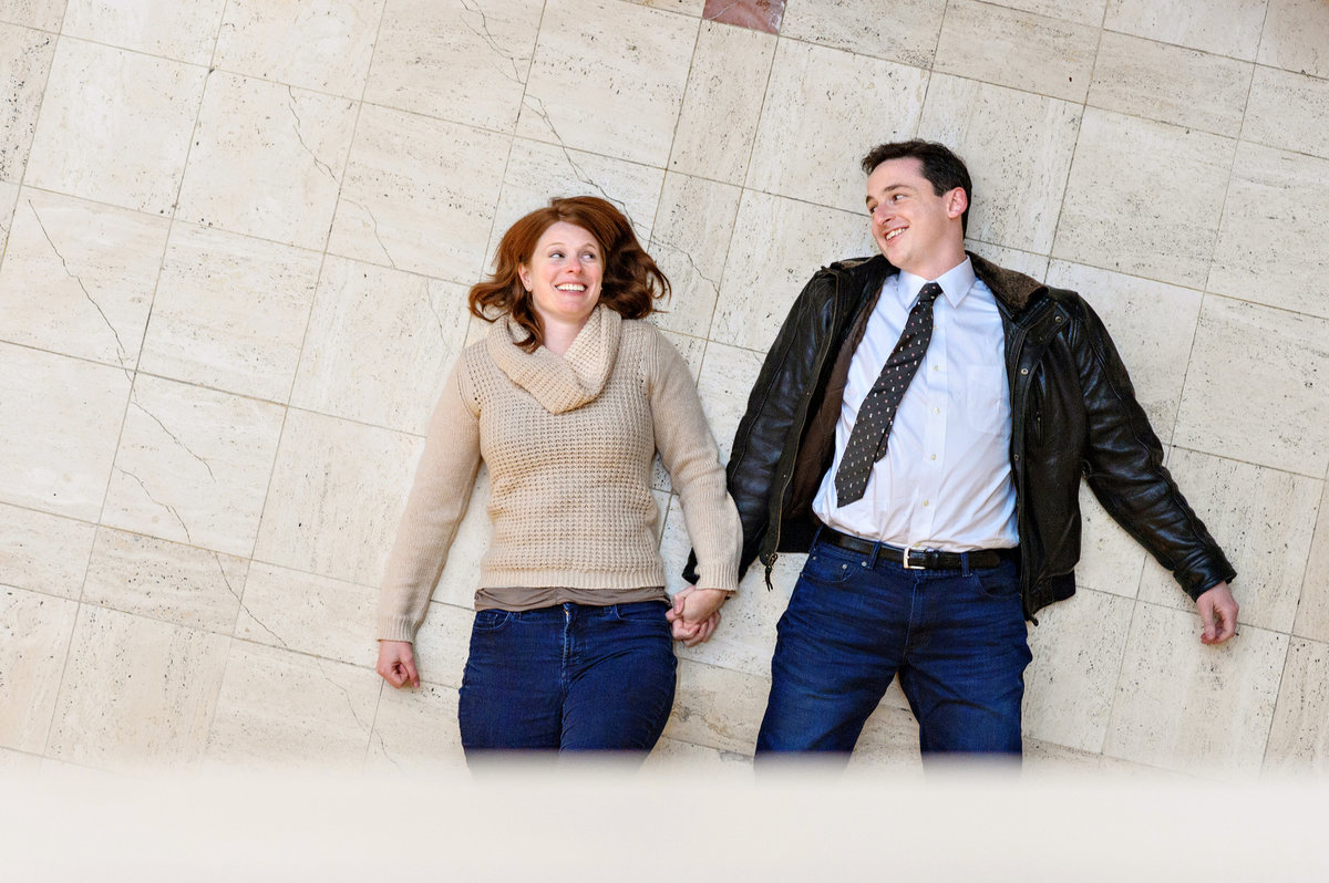 A funny couple lay on the floor of their hotel after a fun engagement session.