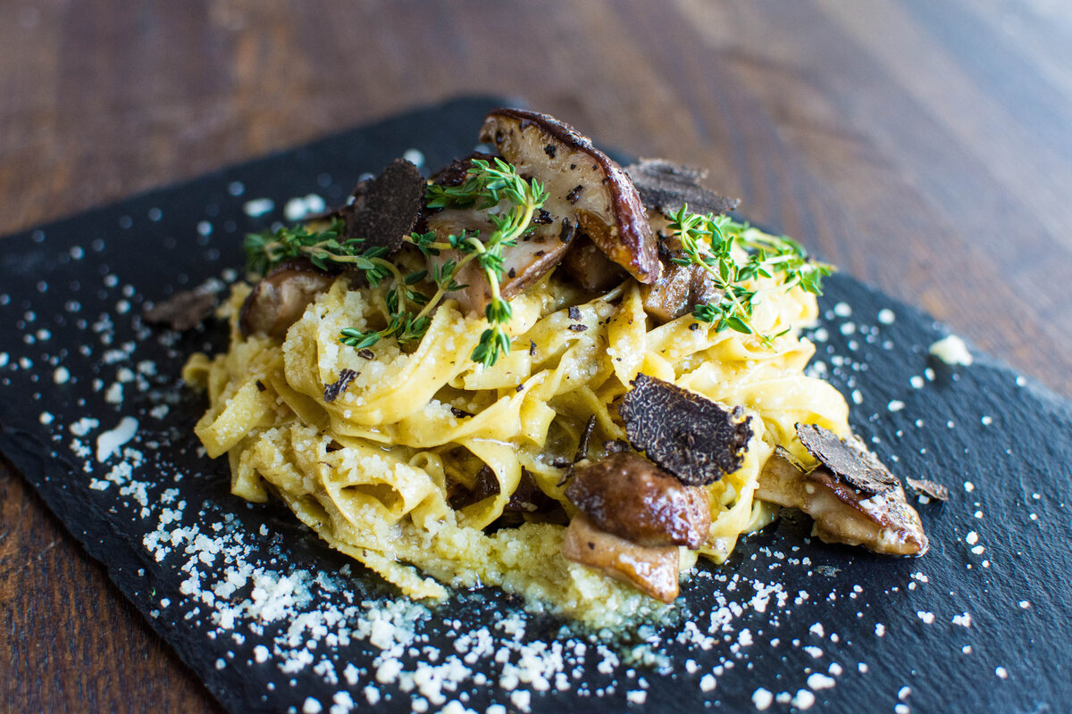 Fresh pasta with mushrooms and truffle oil on a black plate on a dark wood table