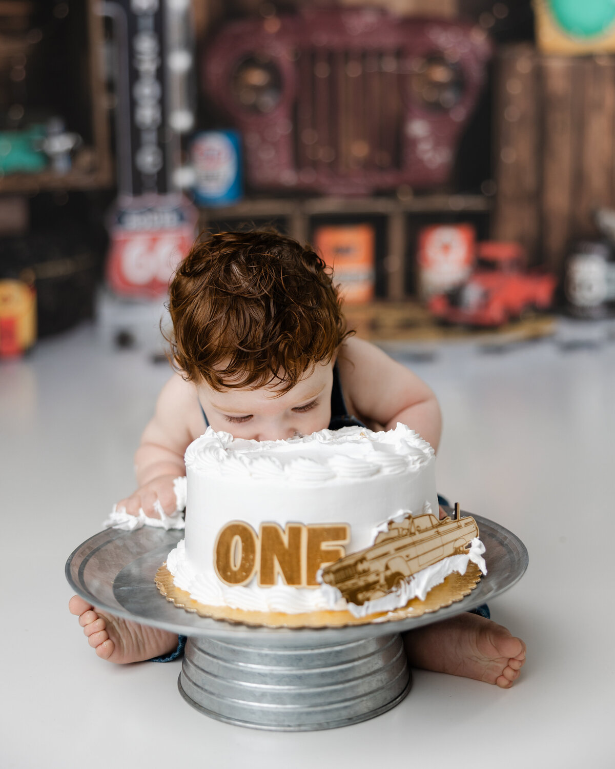 Baby boy digging into his birthday cake headfirst during a rustic, automotive-themed first birthday shoot.
Photograph by Yucaipa cake smash photographer Kaitlyn Dawn Photography.