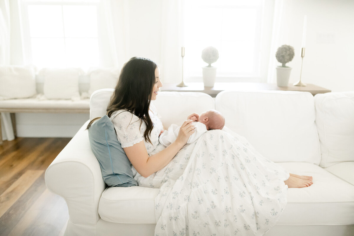 a mother relaxing on her white couch with her newborn baby