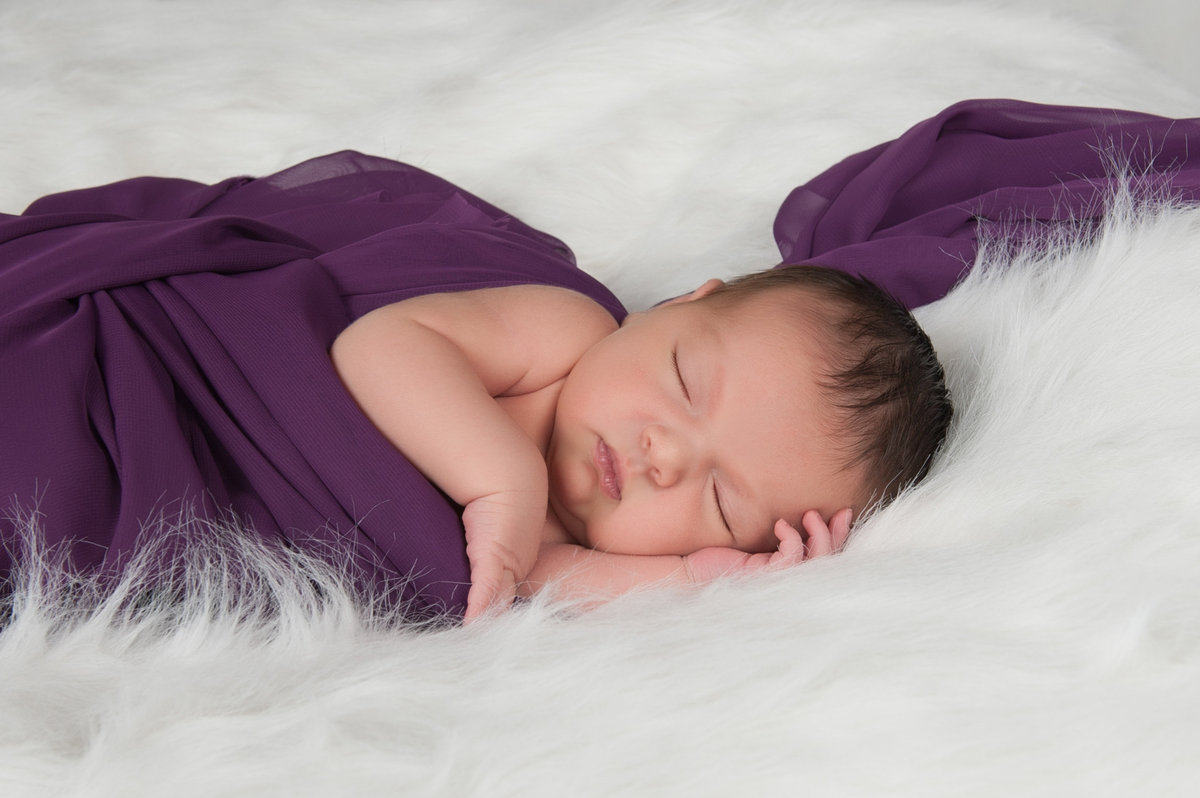 newborn wrapped in purple on white fur