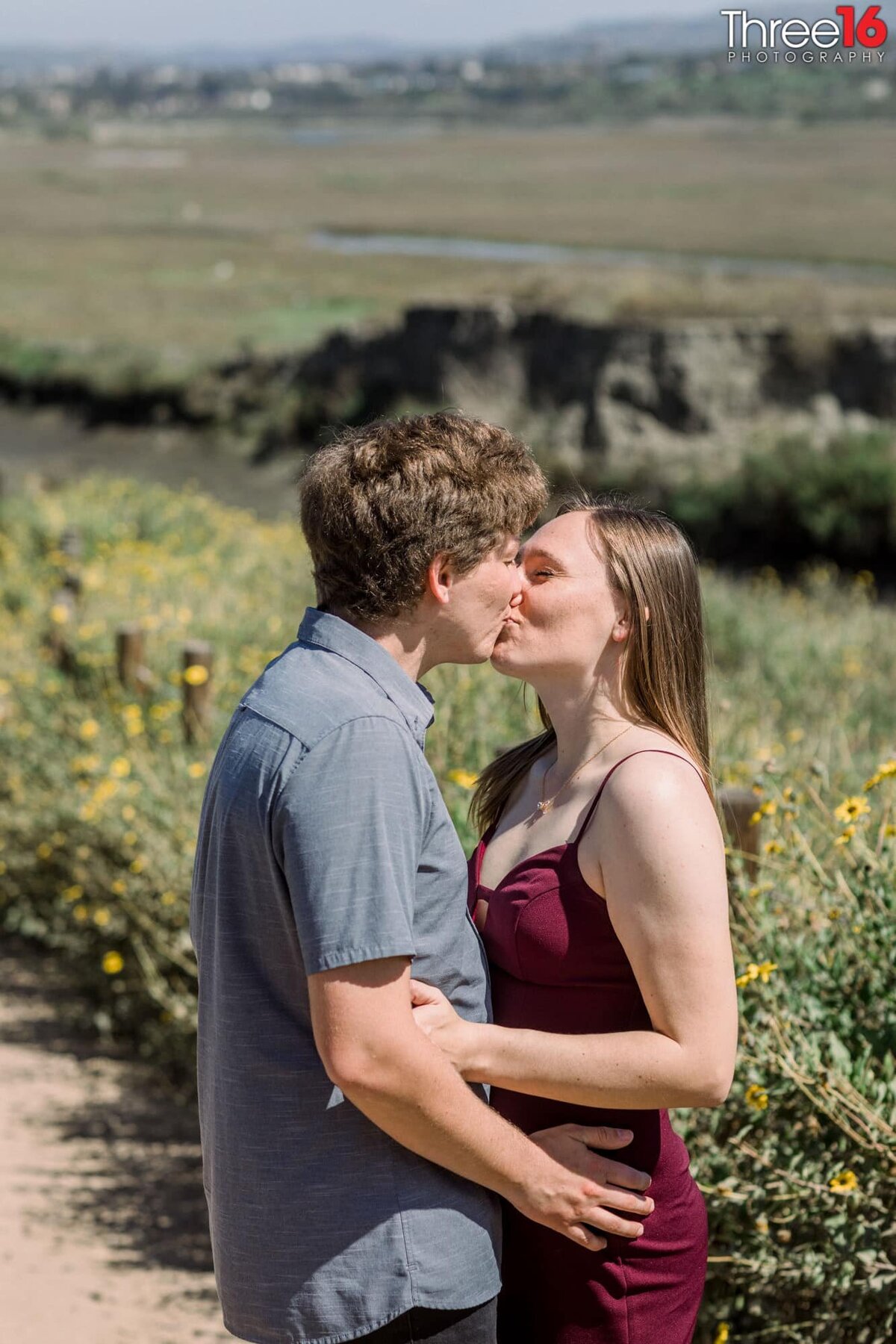 Engaged couple share a sweet kiss amongst the wildflowers along a Upper Newport Bay Nature Preserve trail