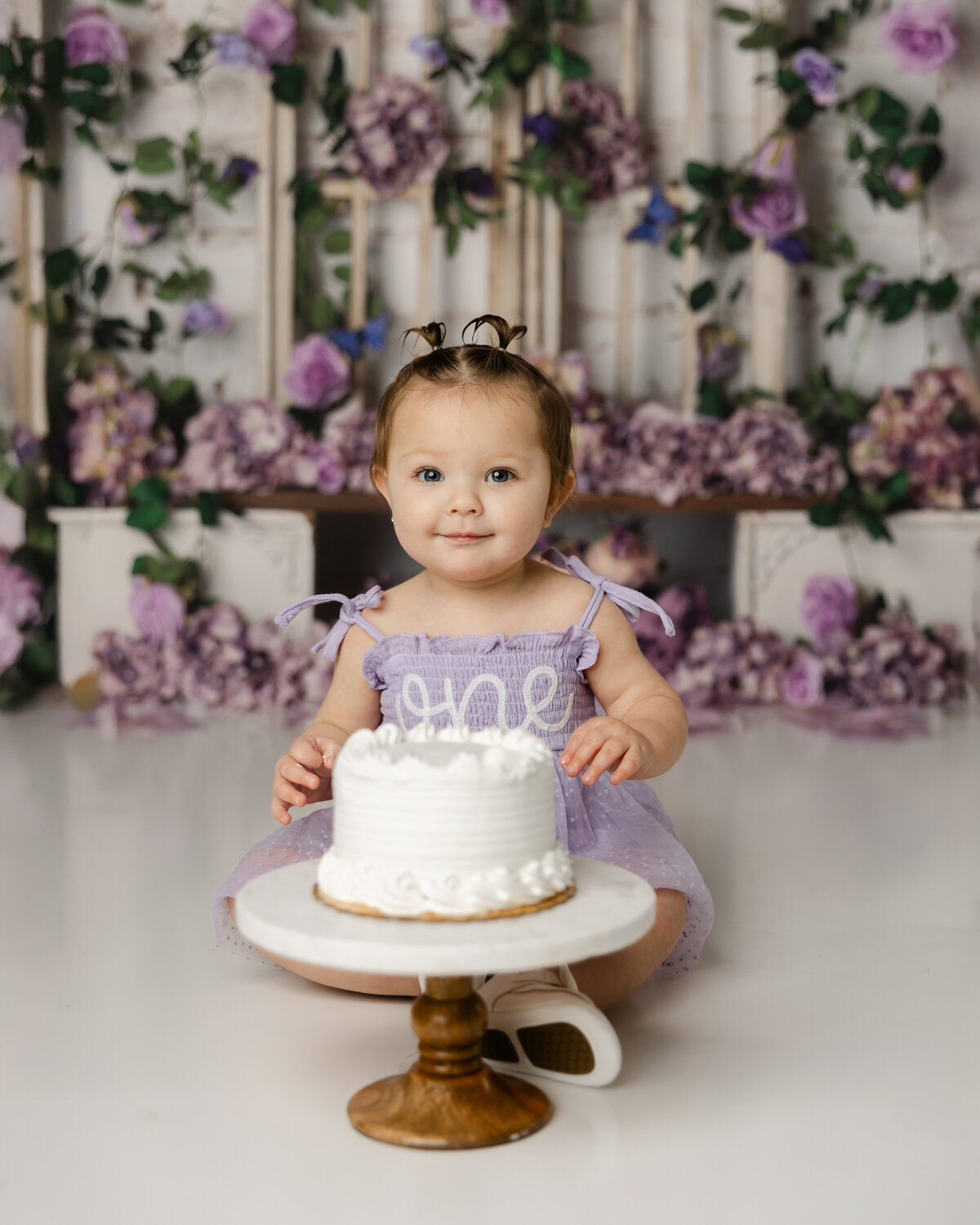 Surrounded by dreamy purple florals, this sweet baby girl celebrated her first big milestone with the most joyful cake smash! Yucaipa cake smash photographer Kaitlyn Dawn Photography.