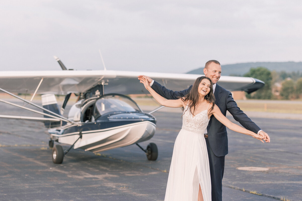 After taking a ride in the plane that this groom build, him and his wife are laughing together while standing at the airport runway snuggled up together watching the sunset during their elopement.