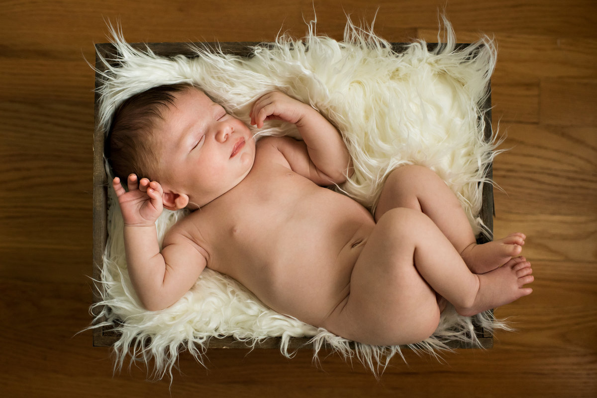 A naked baby laying in a box .