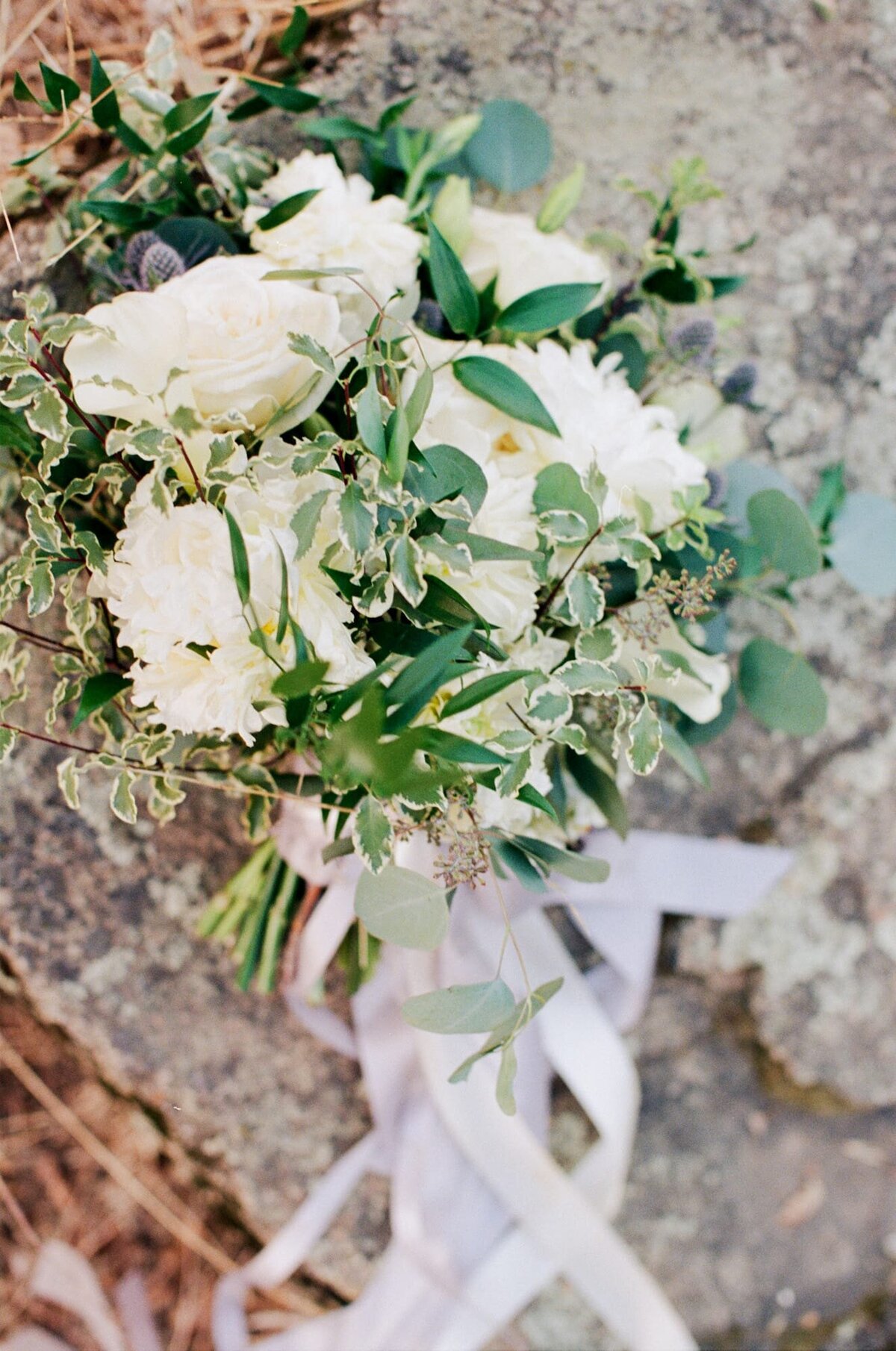 White flowers with leaves and branches tied neatly into a bouquet with silky white ribbons.