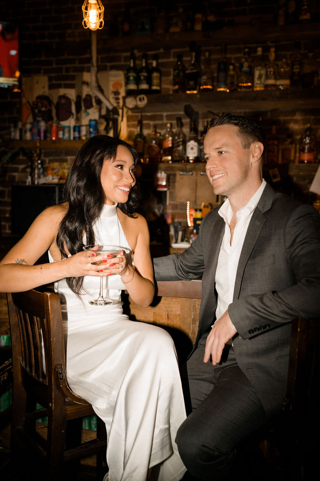 bride and groom sitting at a bar while the bride has a martini glass in her hand