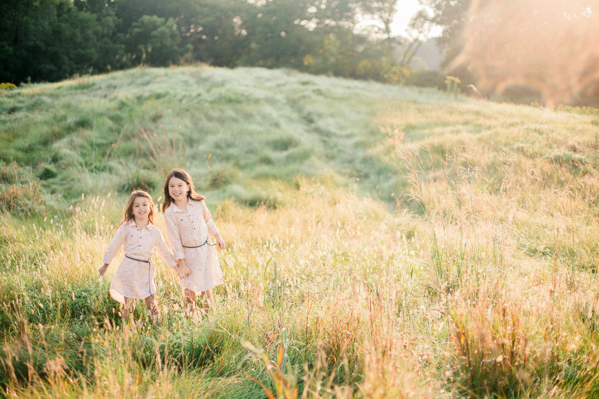 sisters run in grass fields in sunrise rochester minnesota