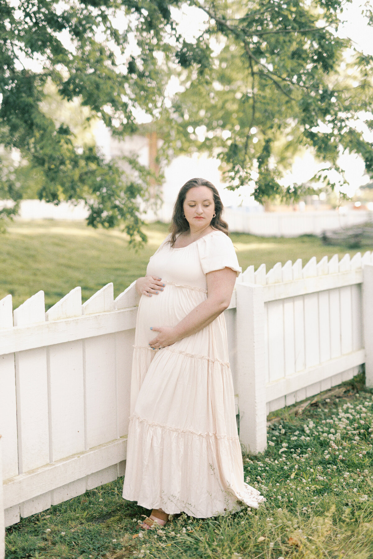 Pregnant woman in cream dress by white fence by Virginia Photographers