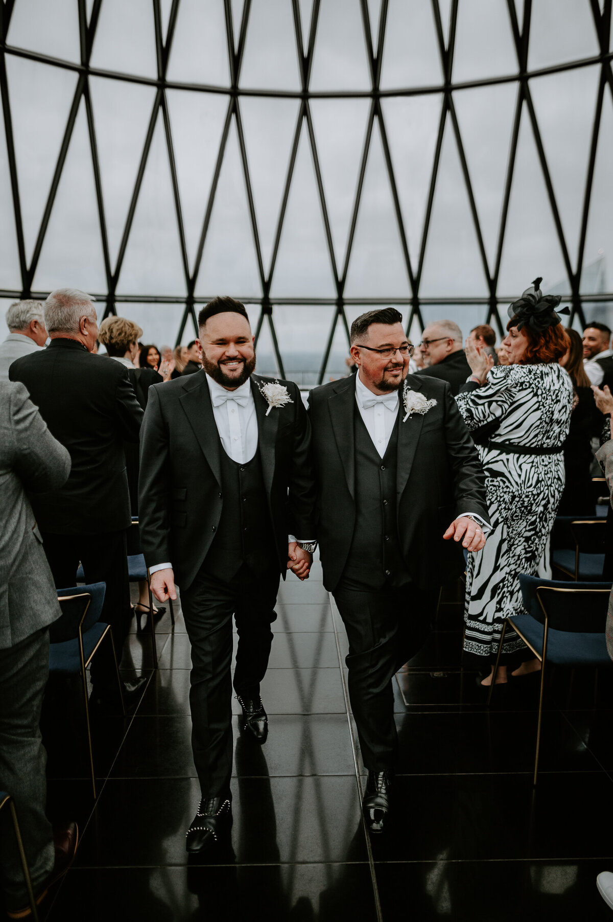 Two grooms get married at The Gherkin in London. They both wore black tie suits and louboutin shoes. The women all wore white dresses and the entire wedding was monochrome apart from the guys red seals.
