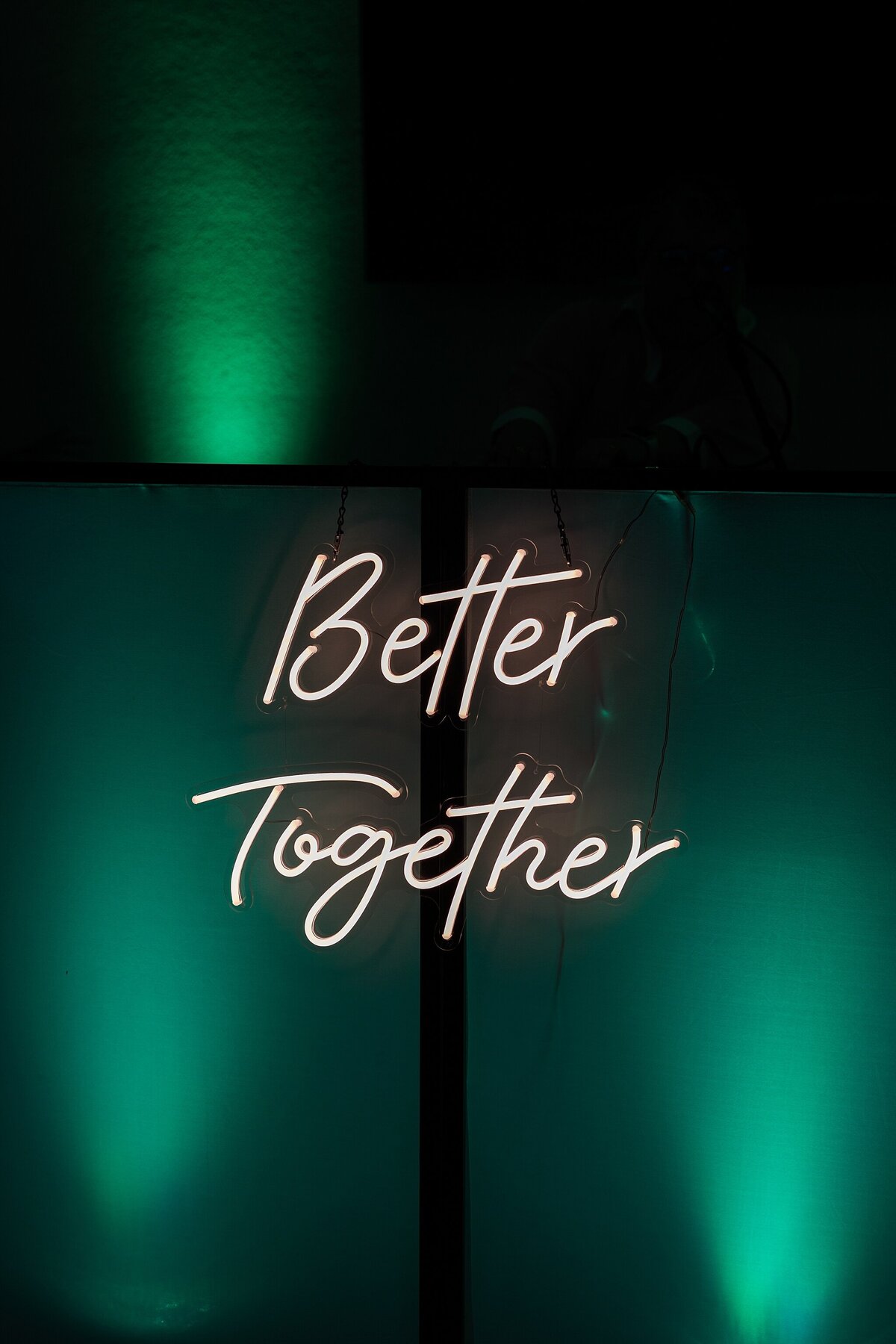 A detail shot of a neon sign reading "Better Together." The sign is bathed in blue green light from multiple floor lights surrounding it.