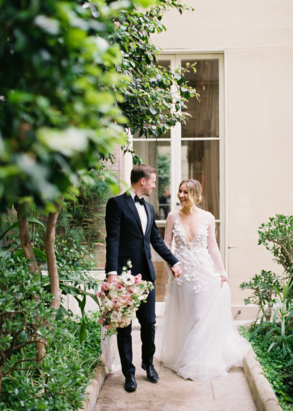 bride wearing tulle wedding dress with flower details walking hands to hands with groom in the orangery