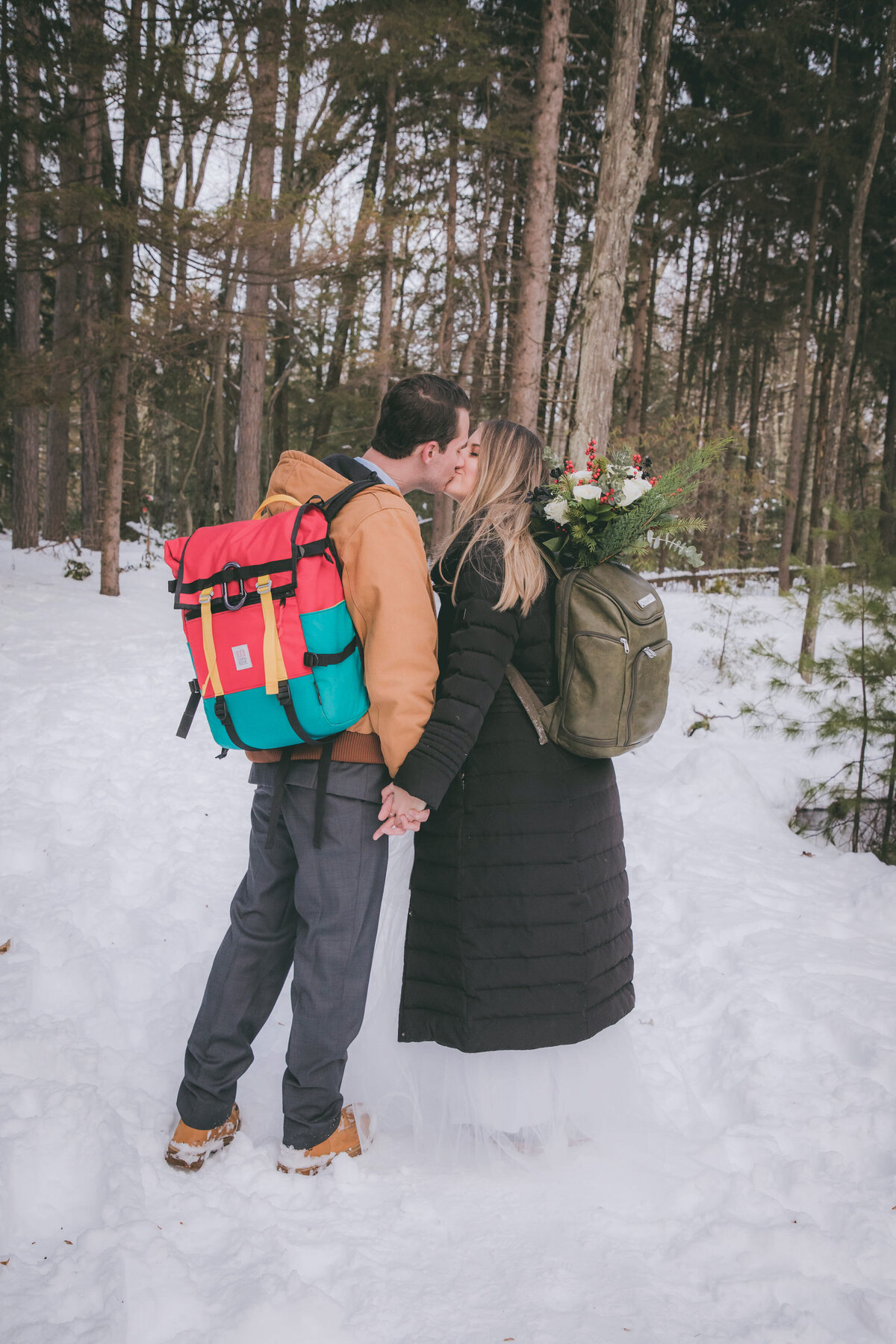 A couple kisses on a snow covered ground during their hiking elopement.