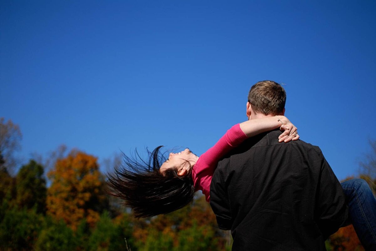 a man spins a woman around in the air in front of clear blue skies as her hair flys