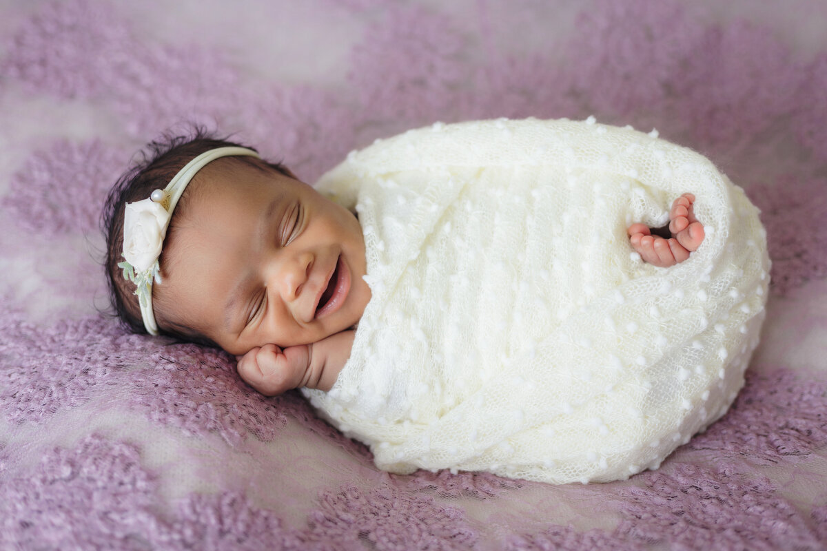 Newborn Photographer, a baby sleeps swaddled in blankets and smiling